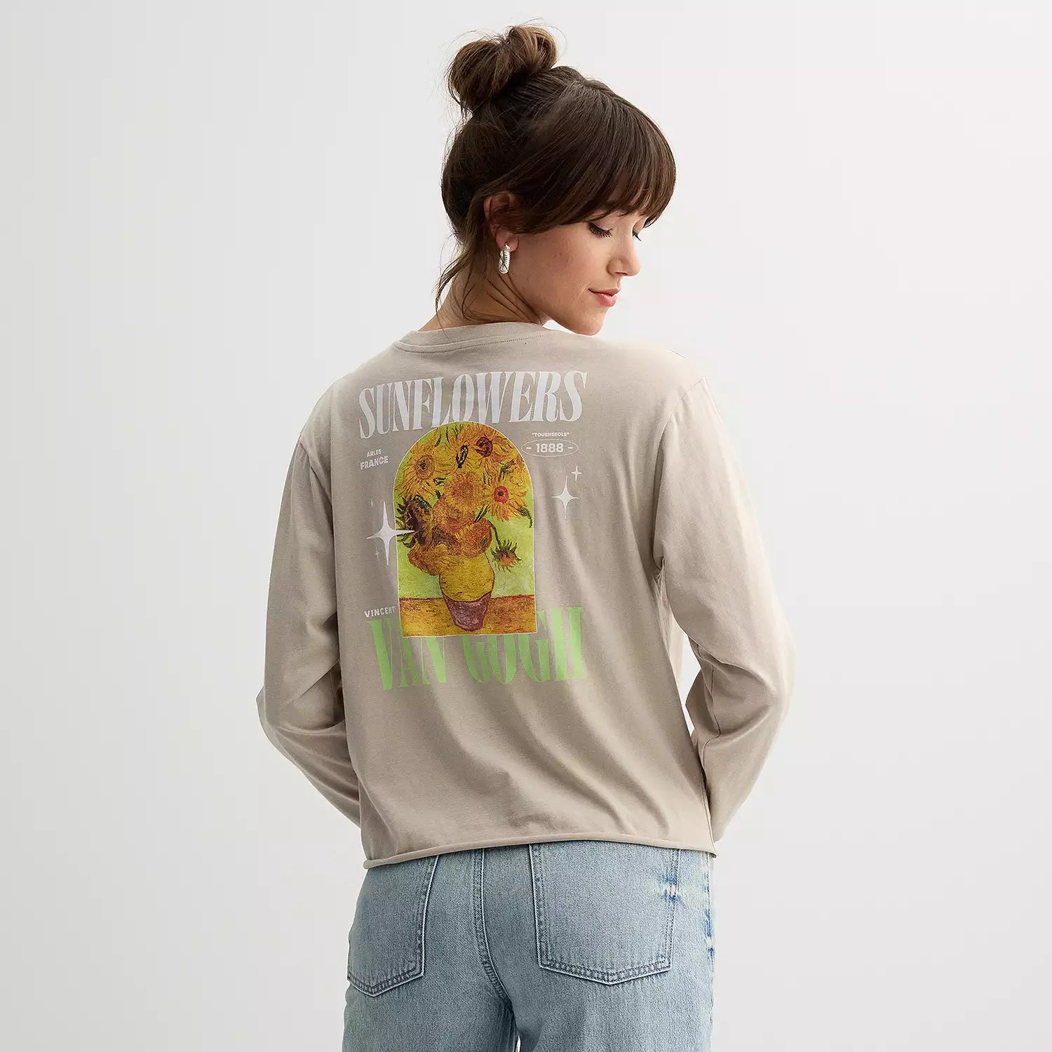 Person wearing a beige long-sleeve shirt with a sunflower graphic and text on the back.