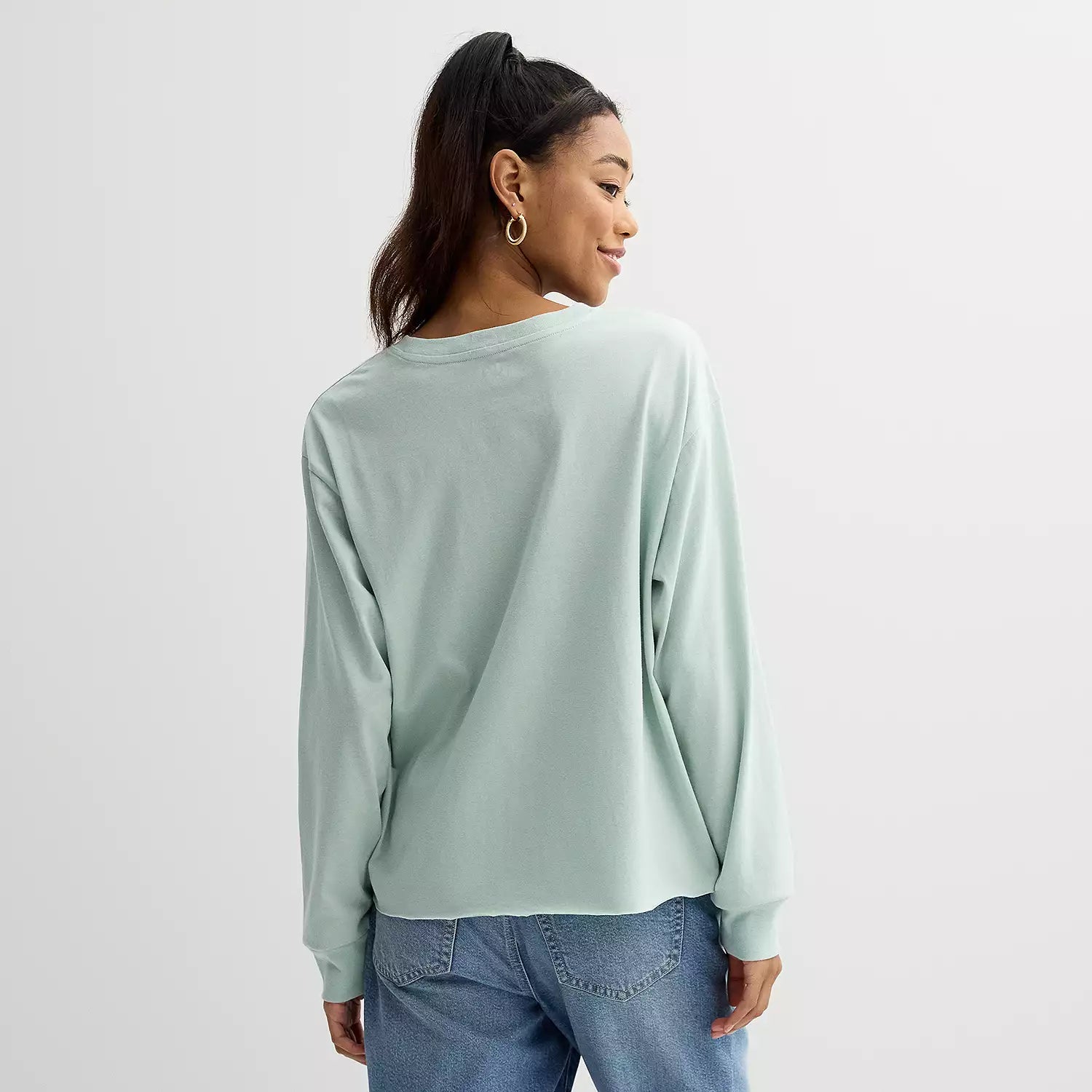 Person wearing a light green long-sleeve shirt and blue jeans on a white background