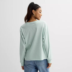 Person wearing a light green long-sleeve shirt and blue jeans on a white background
