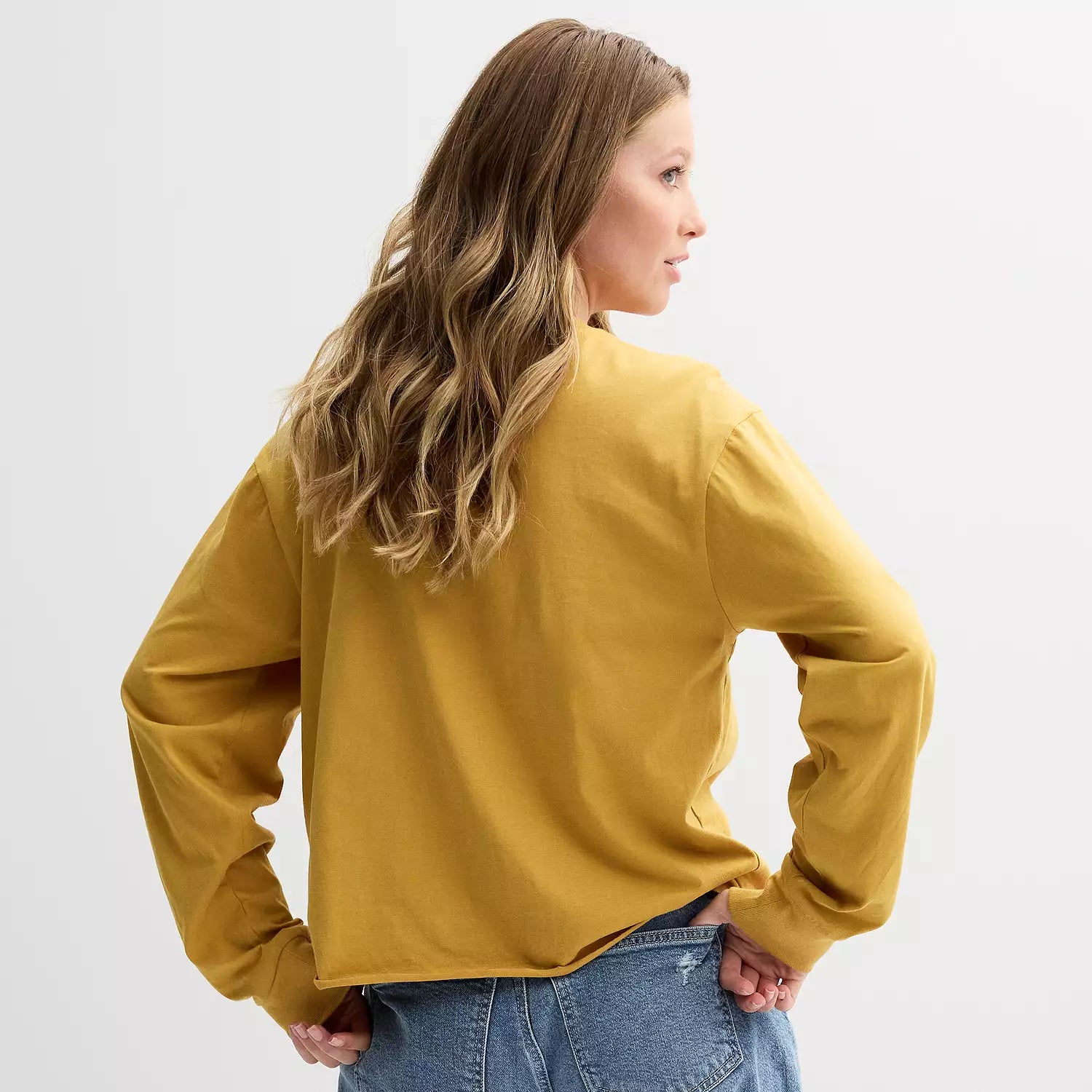 Woman wearing a mustard yellow long-sleeve top on a light gray background
